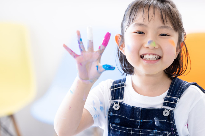 手や顔に絵具をつけて楽しそうに笑う子ども