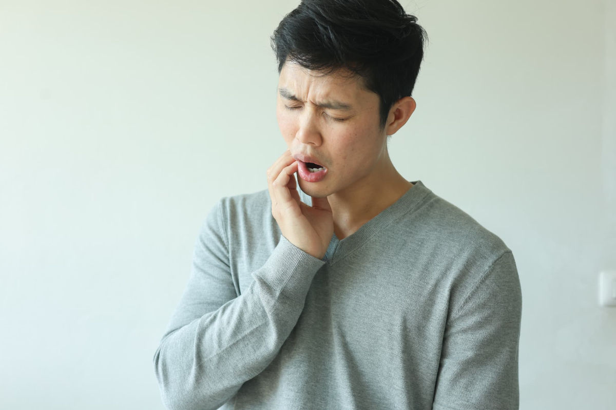 親知らずが生えて口が開きにくくなり顔をしかめる男性
